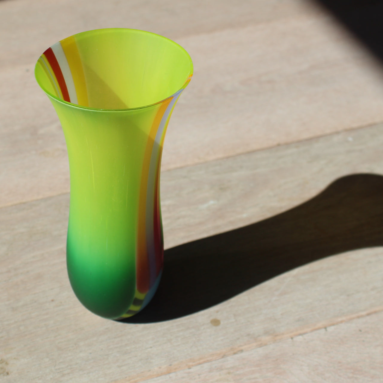 Narrow vibrant coloured glass vase in tones of green, yellow, blue and orange by glass artist Ruth Shelley