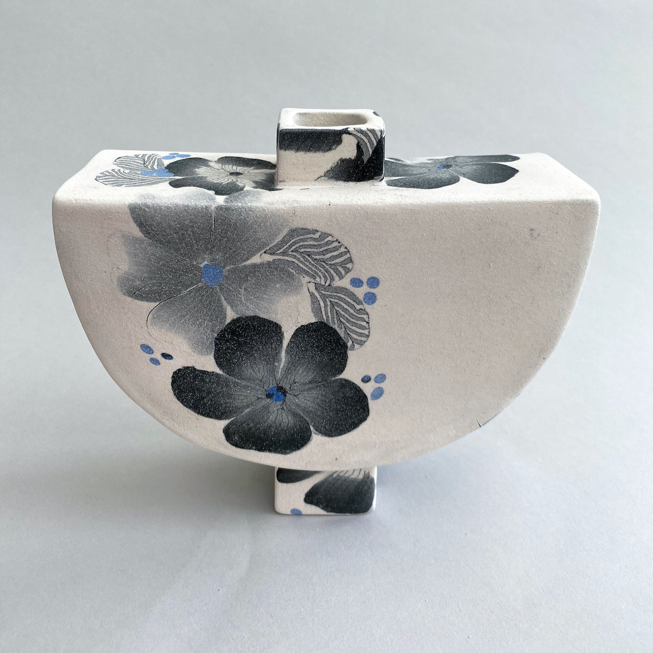 White background semi circular bottle with black, grey and blue floral detail by Judy McKenzie