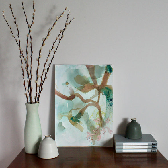 Tara Leaver abstract painting of brown and green seaweed propped on a wooden table next to ceramic vases and three books