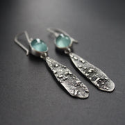 a pair of long lozenge shaped textured silver earrings with pale blue aquamarine stone setting by Carin Lindberg.