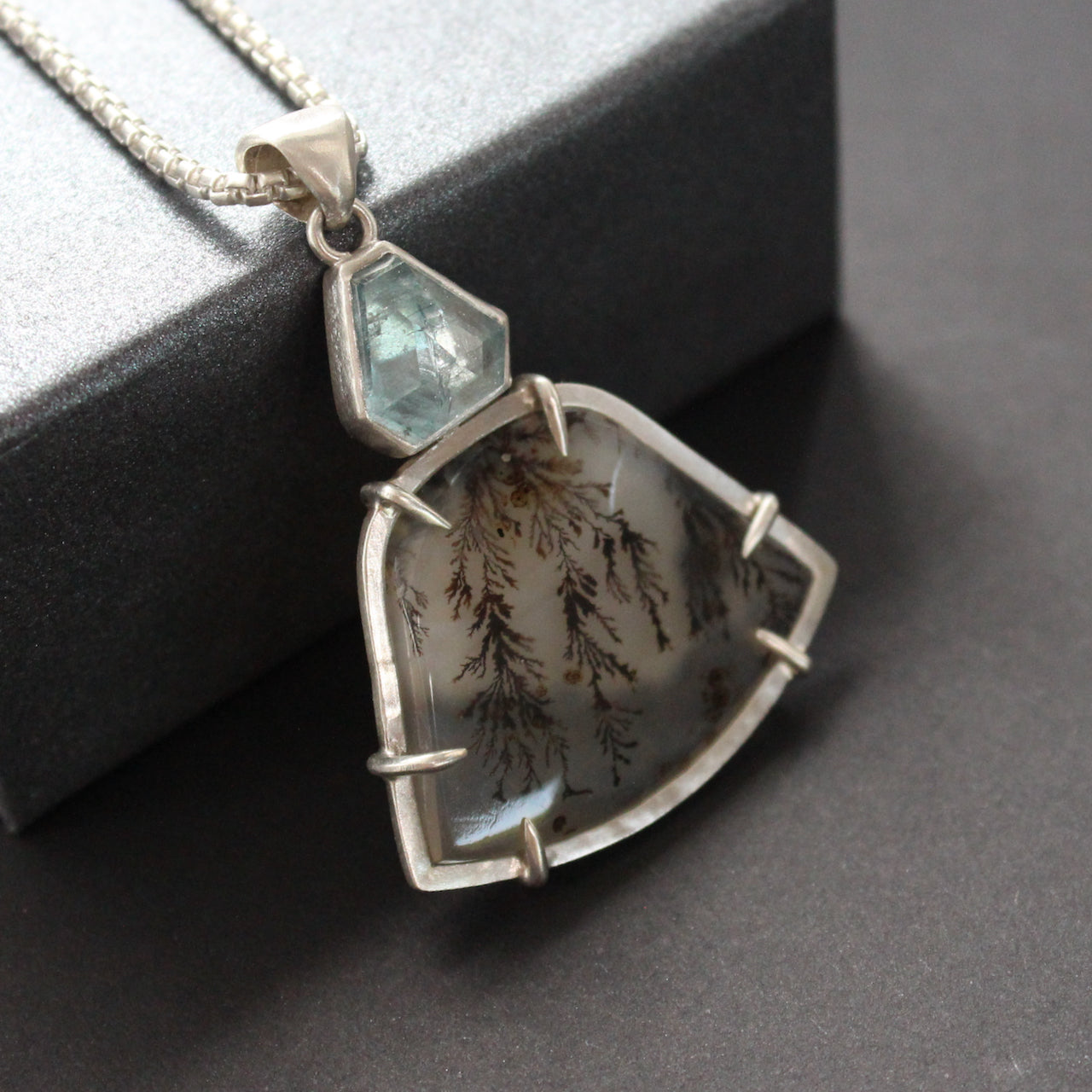 a striking pendant by jewellery designer Carin Lindberg featuring small pale blue stone above a grey and detailed agate stone in a silver setting with clasps