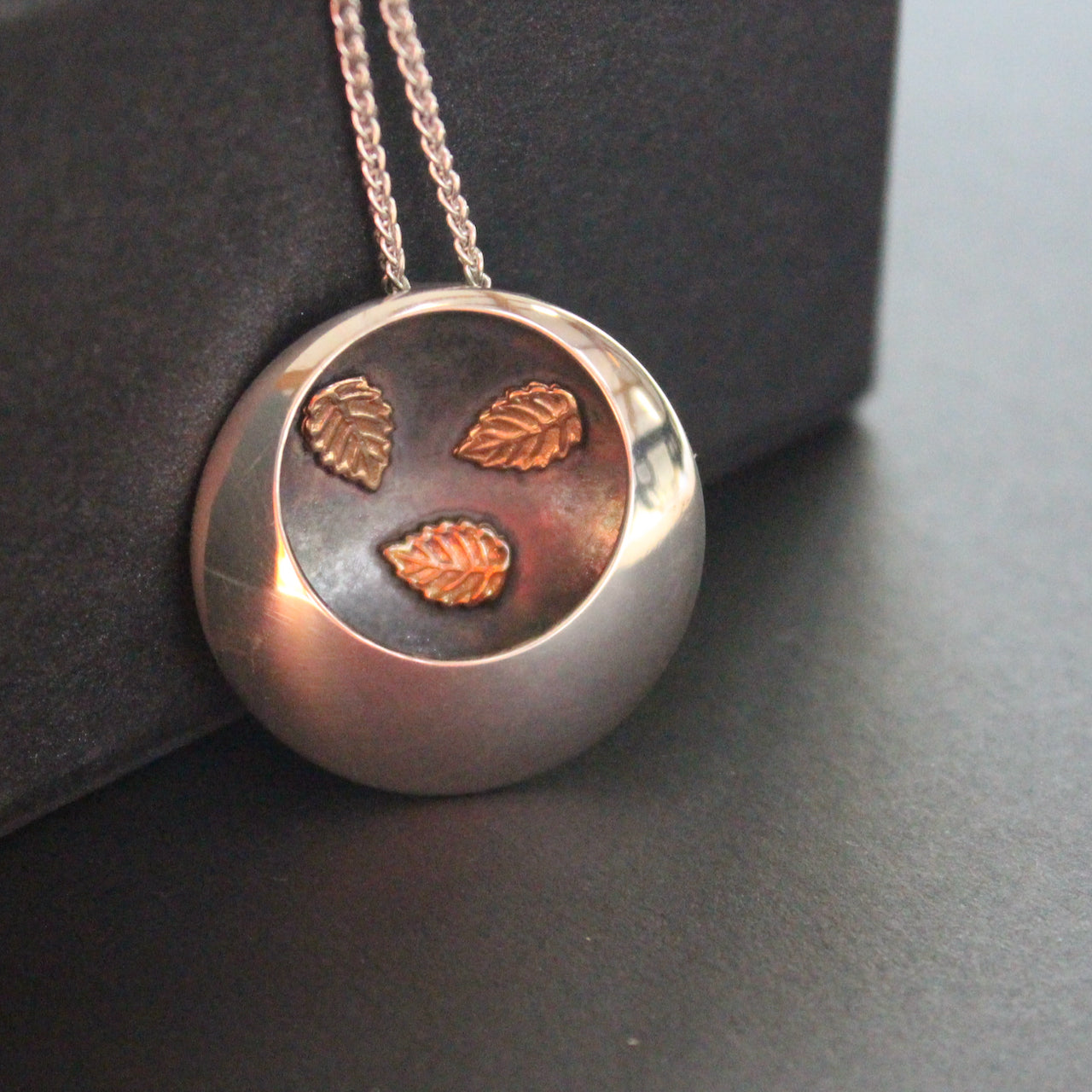 Silver round pendant with 3 inlayed leaves by artist Beverly Bartlett.