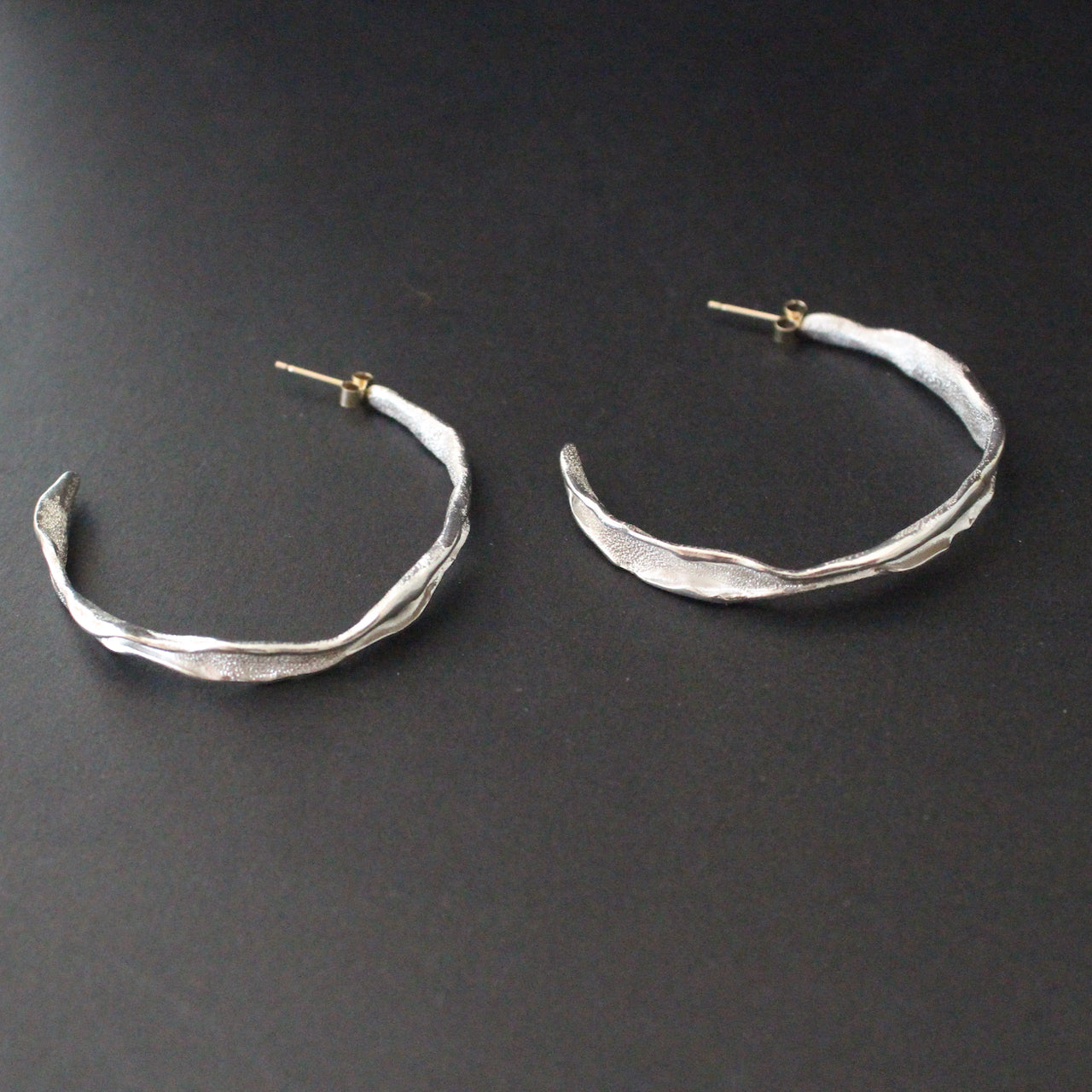 Organically hand sculpted silver Sea Siren hoop earrings, with delicate hand crafted surface detail and gold earring posts by Claire Stockings-Baker