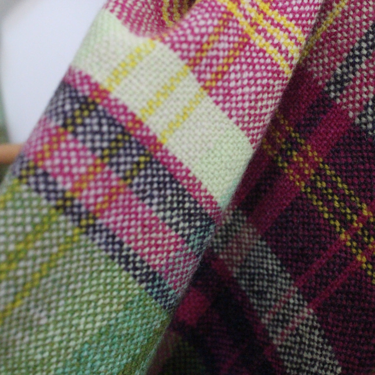 close up of a Teresa Dunne handwoven lambswool scarf in deep pink, pale green and yellow.