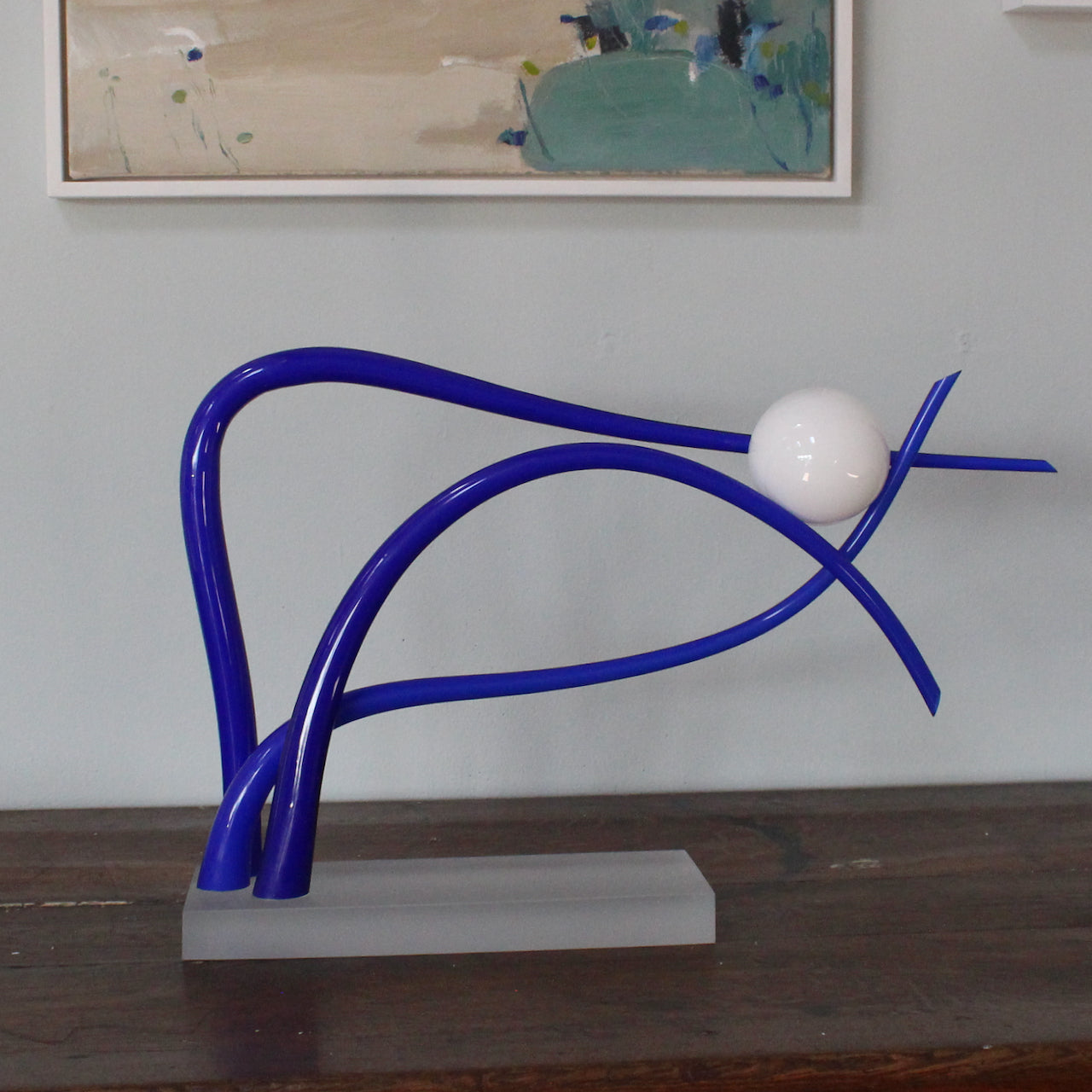 glass sculpture of three blue waves supporting a white ball by Benjamin Lintell