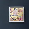 Framed square painting with gold background, bullfinch in foreground amongst branches and pink blossom by artist Jill Hudson