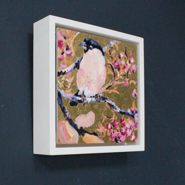 Framed square painting with gold background, bullfinch in foreground amongst branches and pink blossom by artist Jill Hudson.
