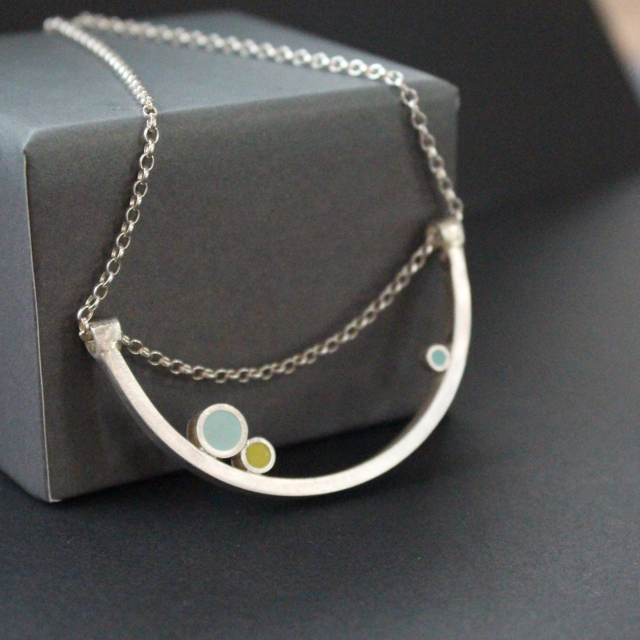 Curved necklace with 3 dots of turquoise, yellow, aqua sitting on curve by UK artist Clare Lloyd