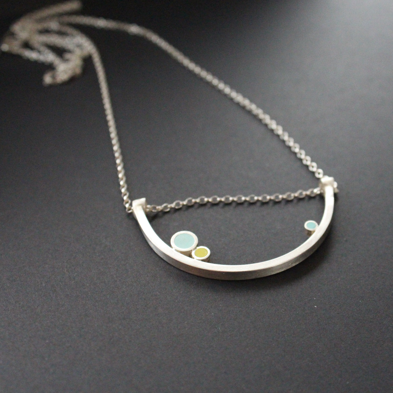 Curved necklace with 3 dots of turquoise, yellow, aqua sitting on curve by artist Clare Lloyd.