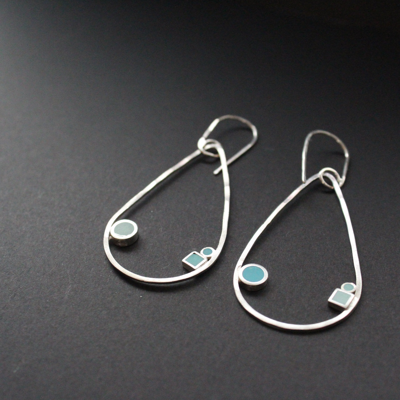 Raindrop shaped drop earrings with round and square dots in turquoise and aqua sitting inside raindrop by artist Clare Lloyd