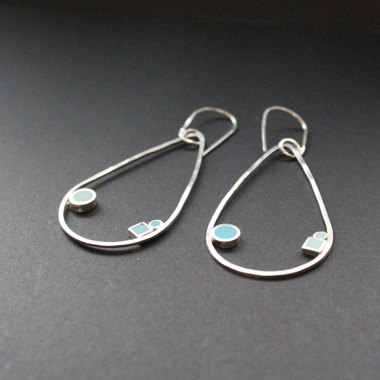 Raindrop shaped drop earrings with round and square dots in turquoise and aqua sitting inside raindrop by artist Clare Lloyd.