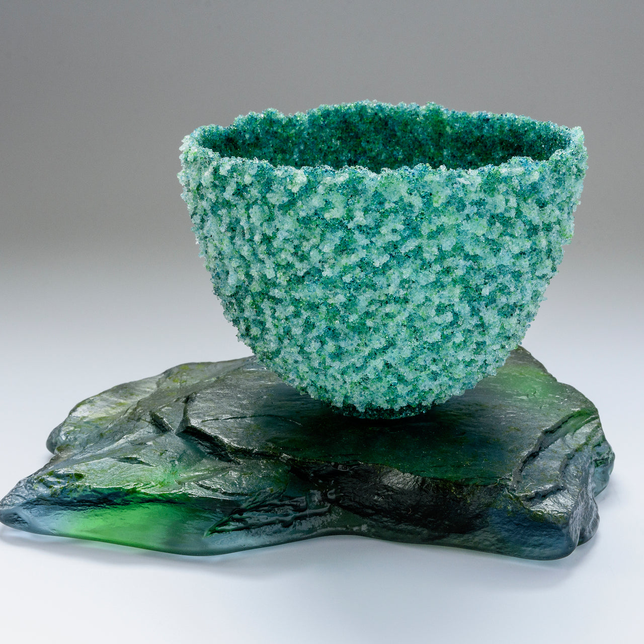 Heavily textured glass vessel sitting on glass slab by artist Caroline Reed