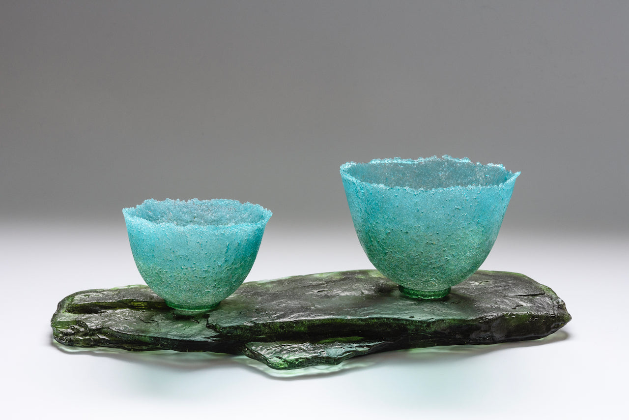 Textured aquamarine glass vessels or two sizes side by side on glass slab by artist Caroline Reed.