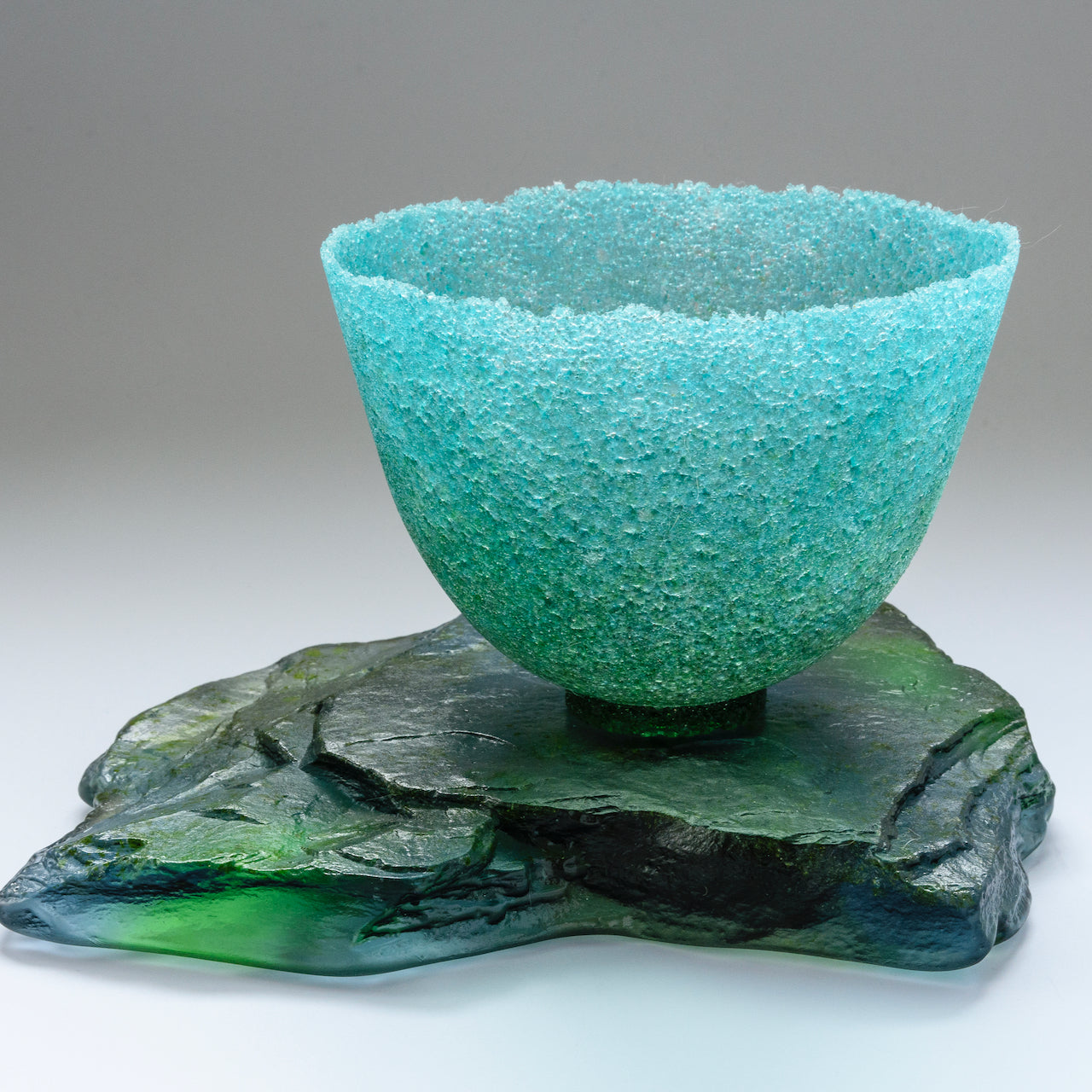 Aquamarine textured glass vessel sitting on glass slab by artist Caroline Reed