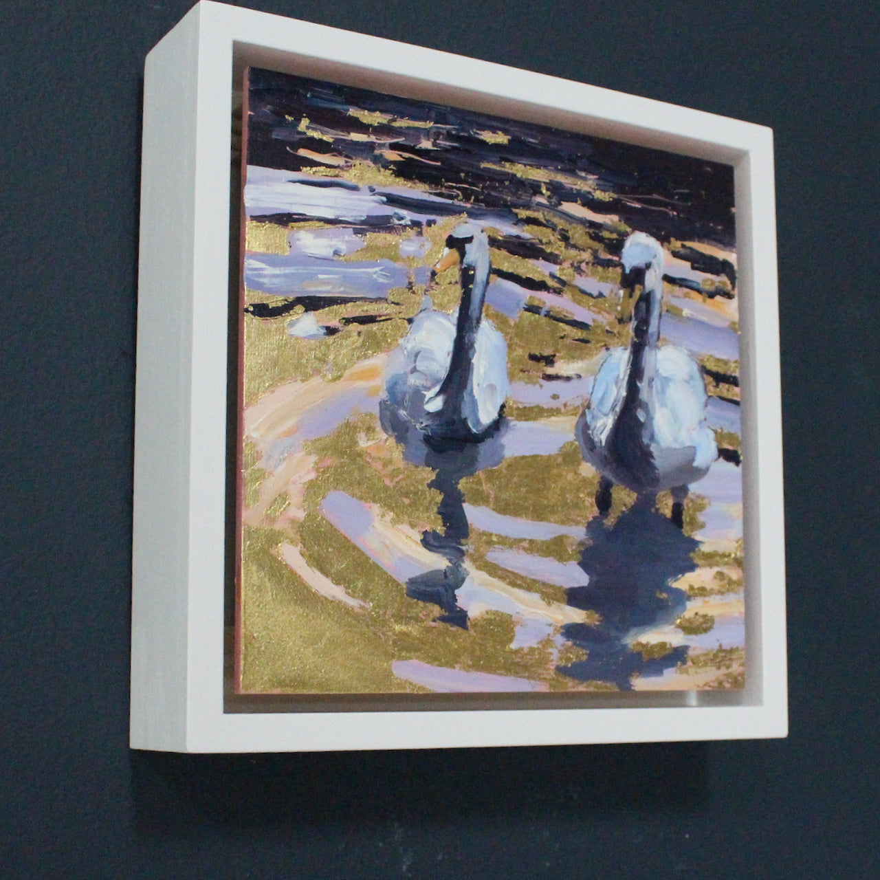 Framed square painting by artist Jill Hudson with gold water reflection and two swans swimming