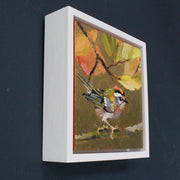 Artist Jill Hudson, gold square background with firecrest on branch in foreground and brown & green leaves.