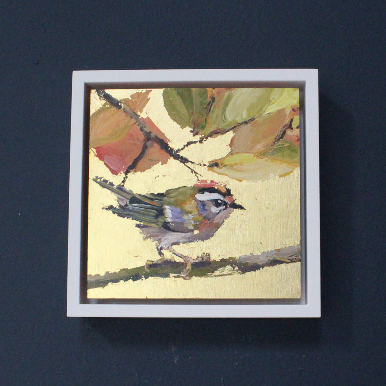 Jill Hudson painting of a firecrest bird on branch in foreground and brown & green leaves.