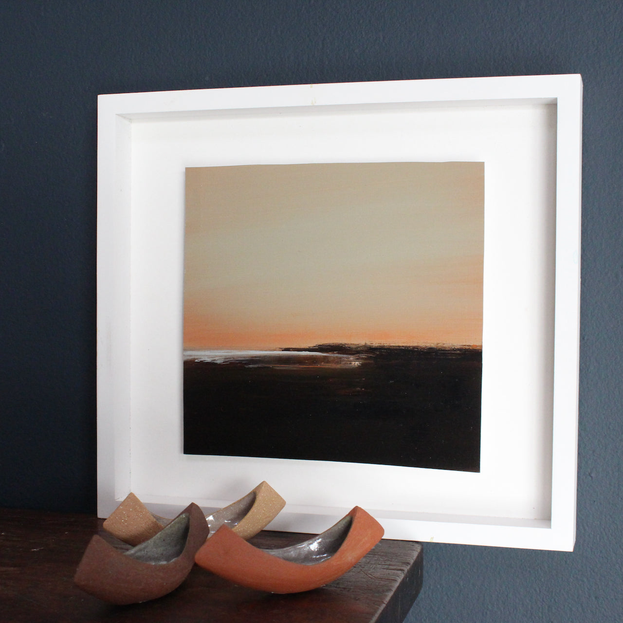 Dusky pink sky with dark tones of the landscape and white shimmering ocean by artist Nicola Mosley.