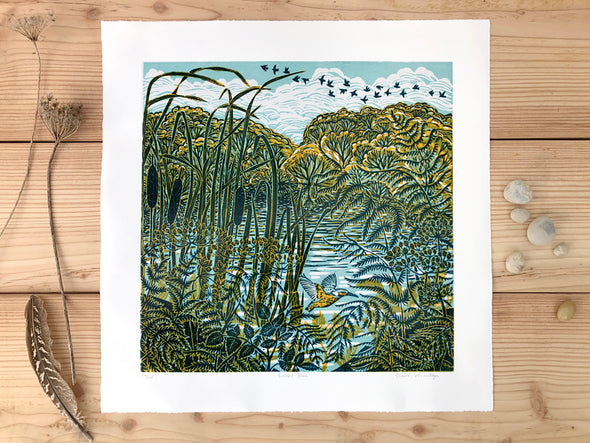 Lino print by Cornish artist Claire Armitage, foliage and bull rush in the foreground with water and trees and sky in background.