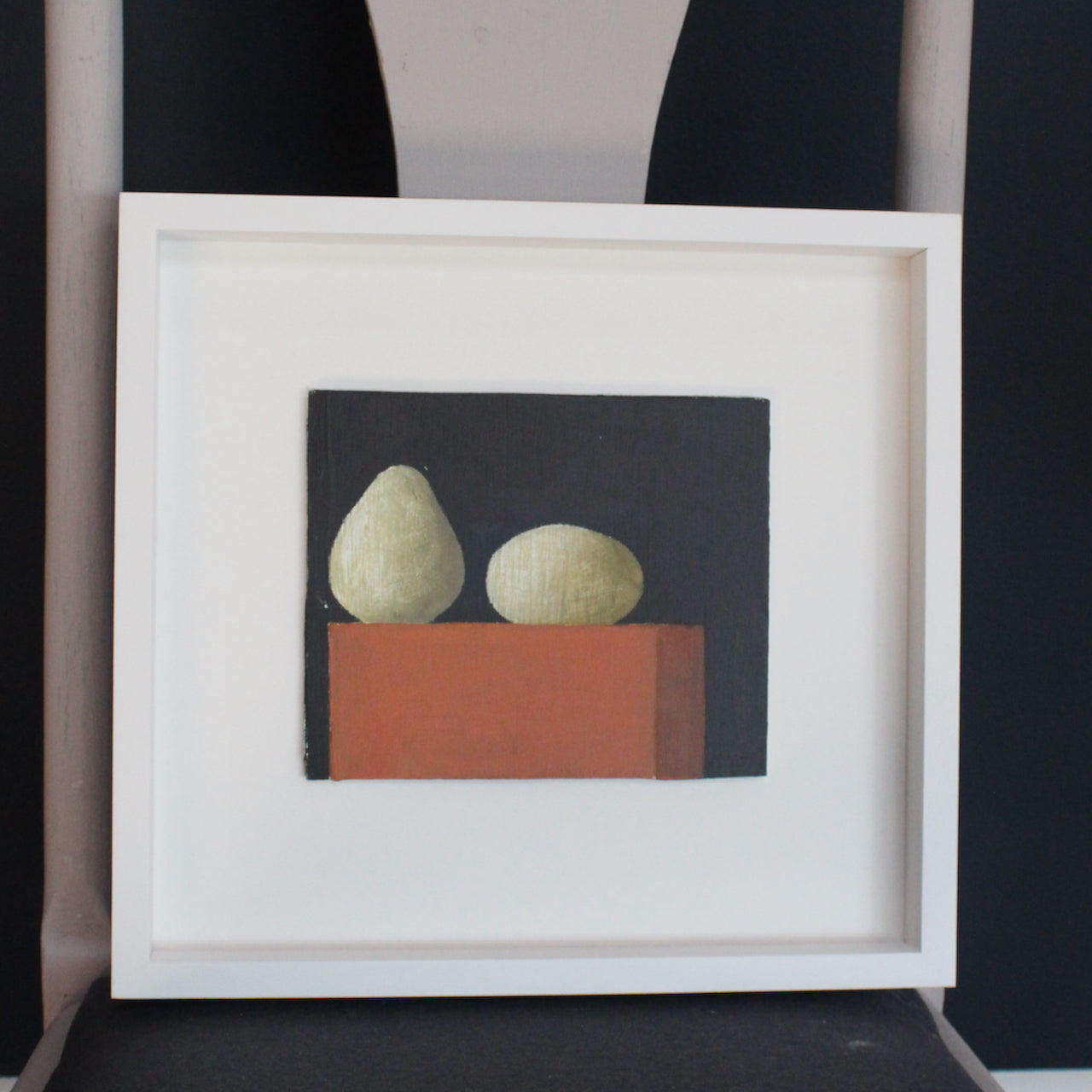 Artist Philip Lyons framed painting of two gourds on an orange brick with black wall behind.