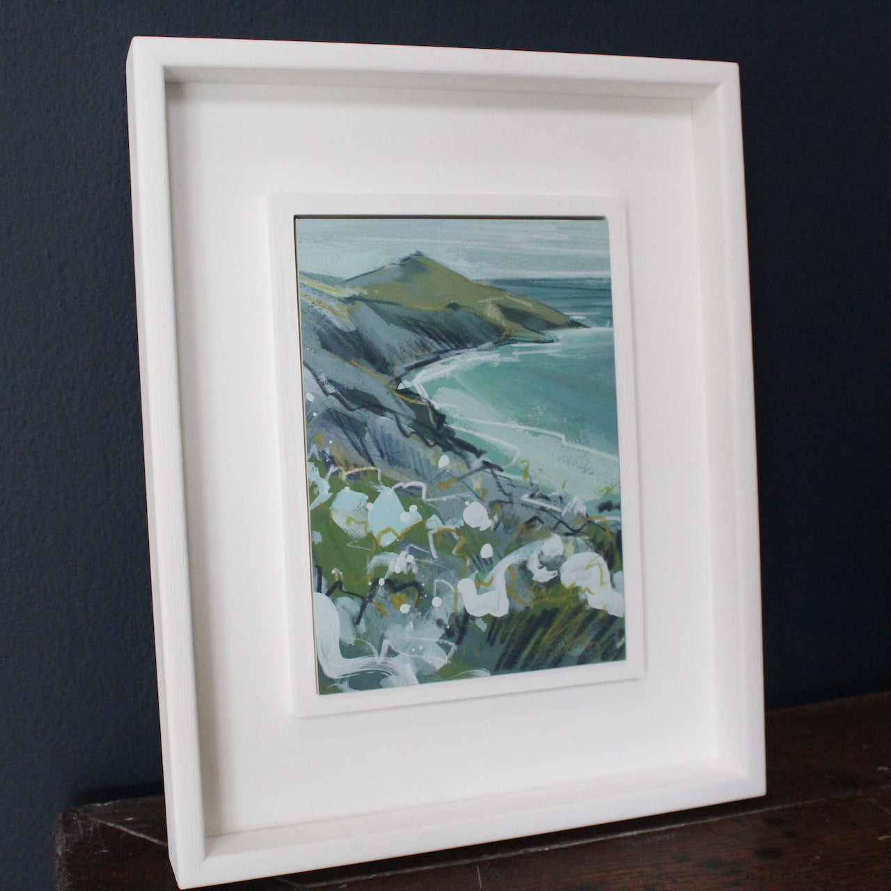 Imogen Bone, Cornish artist. Small painting, the sea is green with hints of white, the peninsula greys, ochre and white flowers