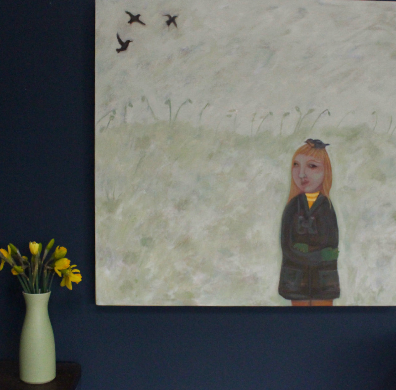 Siobhan Purdy painting of a girl with long blonde hair wearing a dark green coast with binoculars round her neck on a dark wall next to a green vase with daffodils in it.