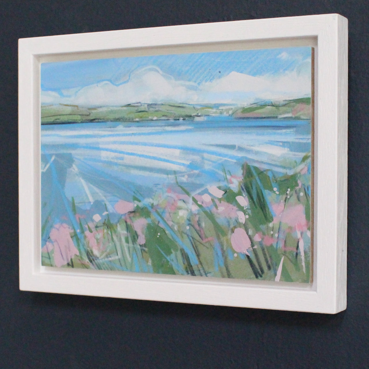 a small framed painting by Imogen Bone,  of river with green hills, pale blue river and pink flowers on the riverbank.