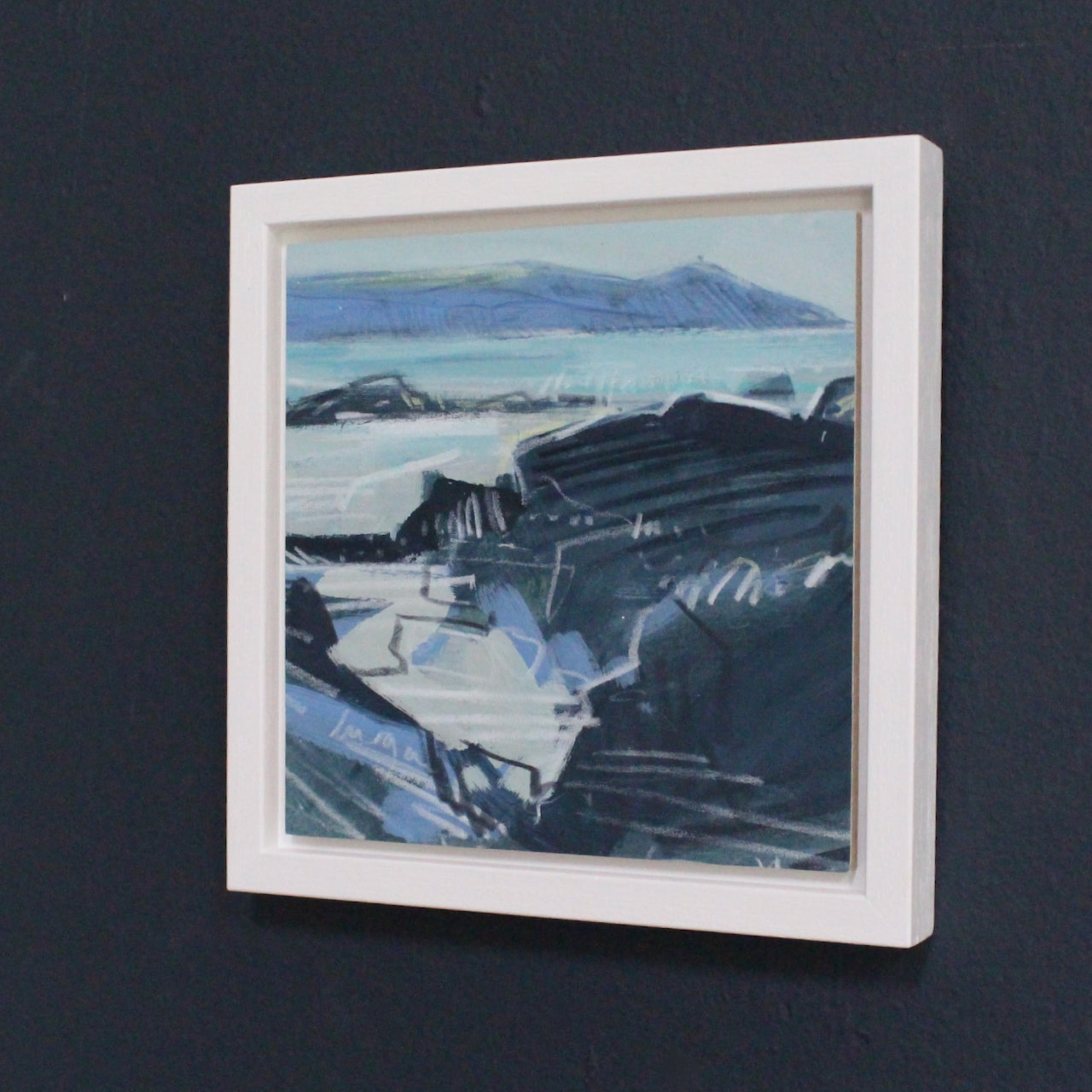 a small framed seascape of Rame Head by Imogen Bone, Cornish artist. The cliffs are shades of blue and black and the sea is pale blue with hints of white and turquoise.