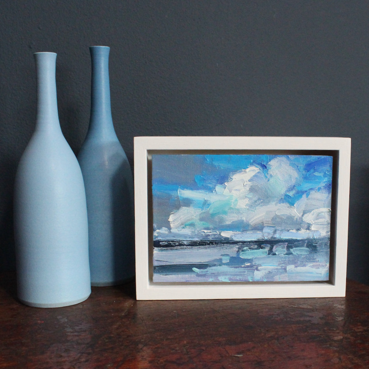 a framed Jill Hudson seascape of a blue and purple sky with white clouds over a grey and blue sea