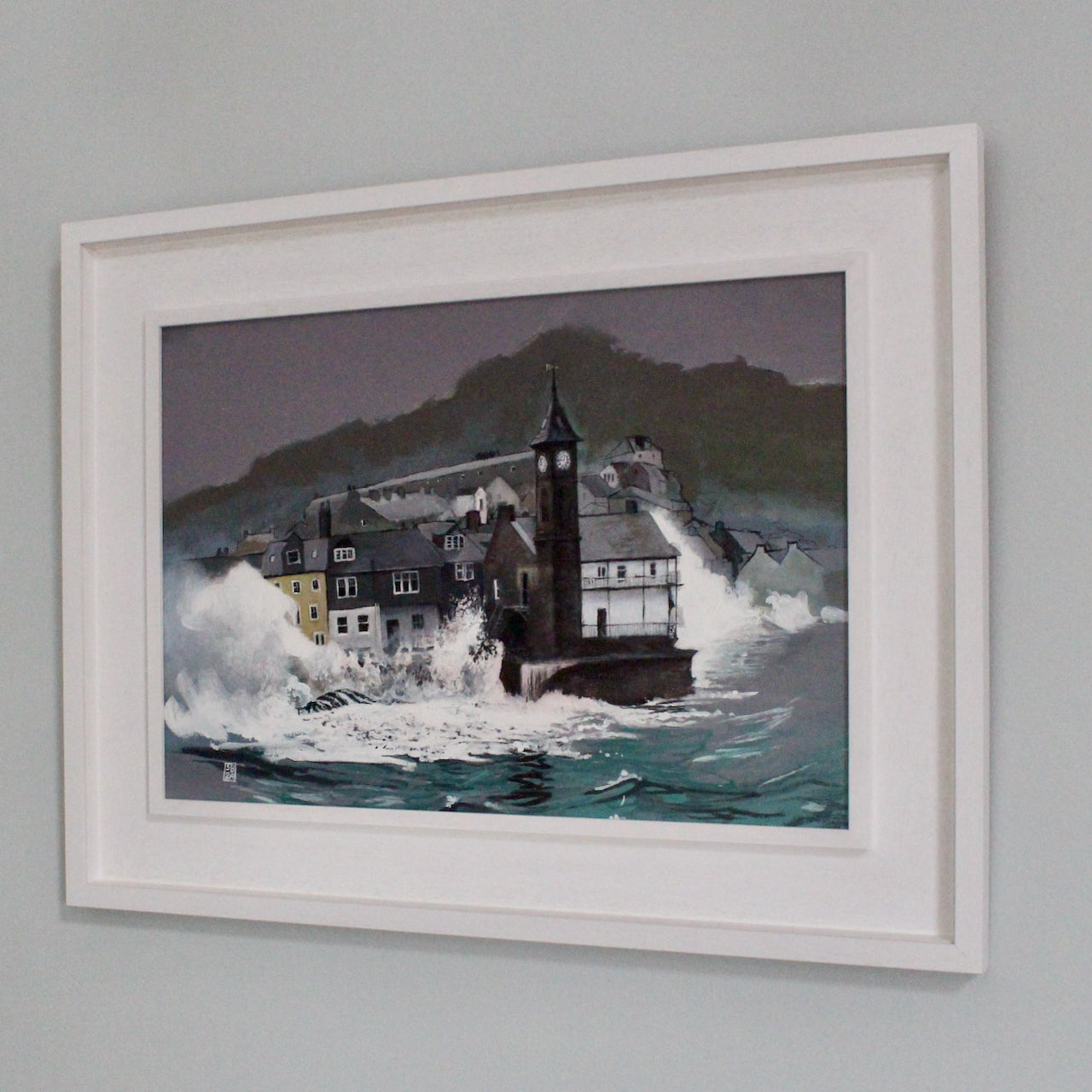 a framed painting of a the Kingsand clocktower in Cornwall with waves crashing against it and the neighbouring buildings it is by Steven Buckler