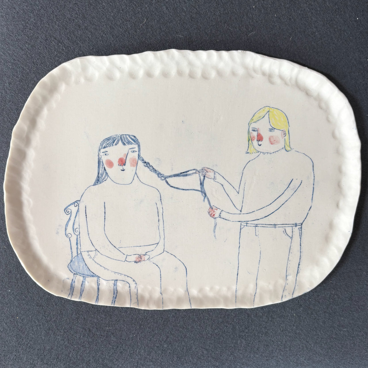 Becca Brown ceramic plaque with line drawing of two women, one putting plaits in the others hair