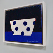 a framed painting by Sophie Harding of white bowl with blue spots on a blue table.