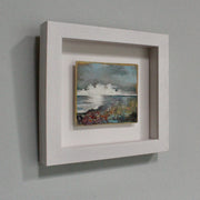 a small framed Julie Ellis seascape painting of white clouds on the horizon of a blue sea with flowers in the foreground.