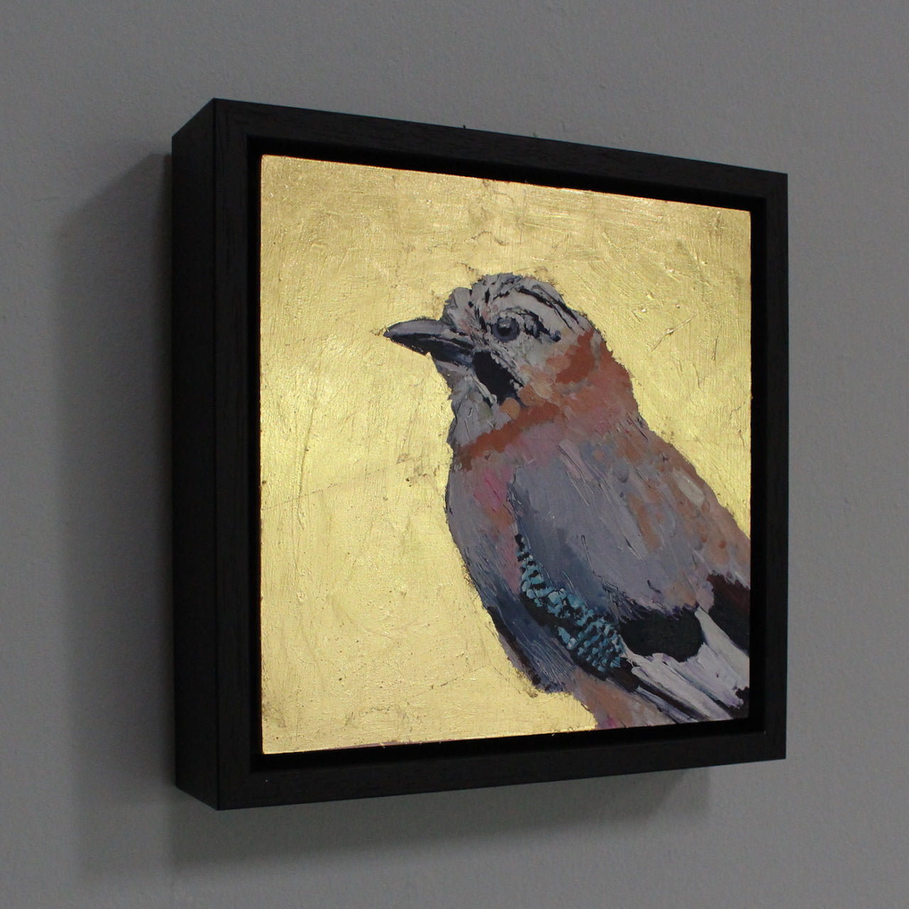 a framed Jill Hudson painting of a jaybird on a gold background.