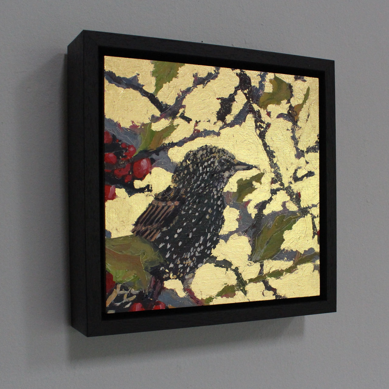 a framed Jill Hudson of a starling on a branch of a tree the background of the painting is gold leaf.