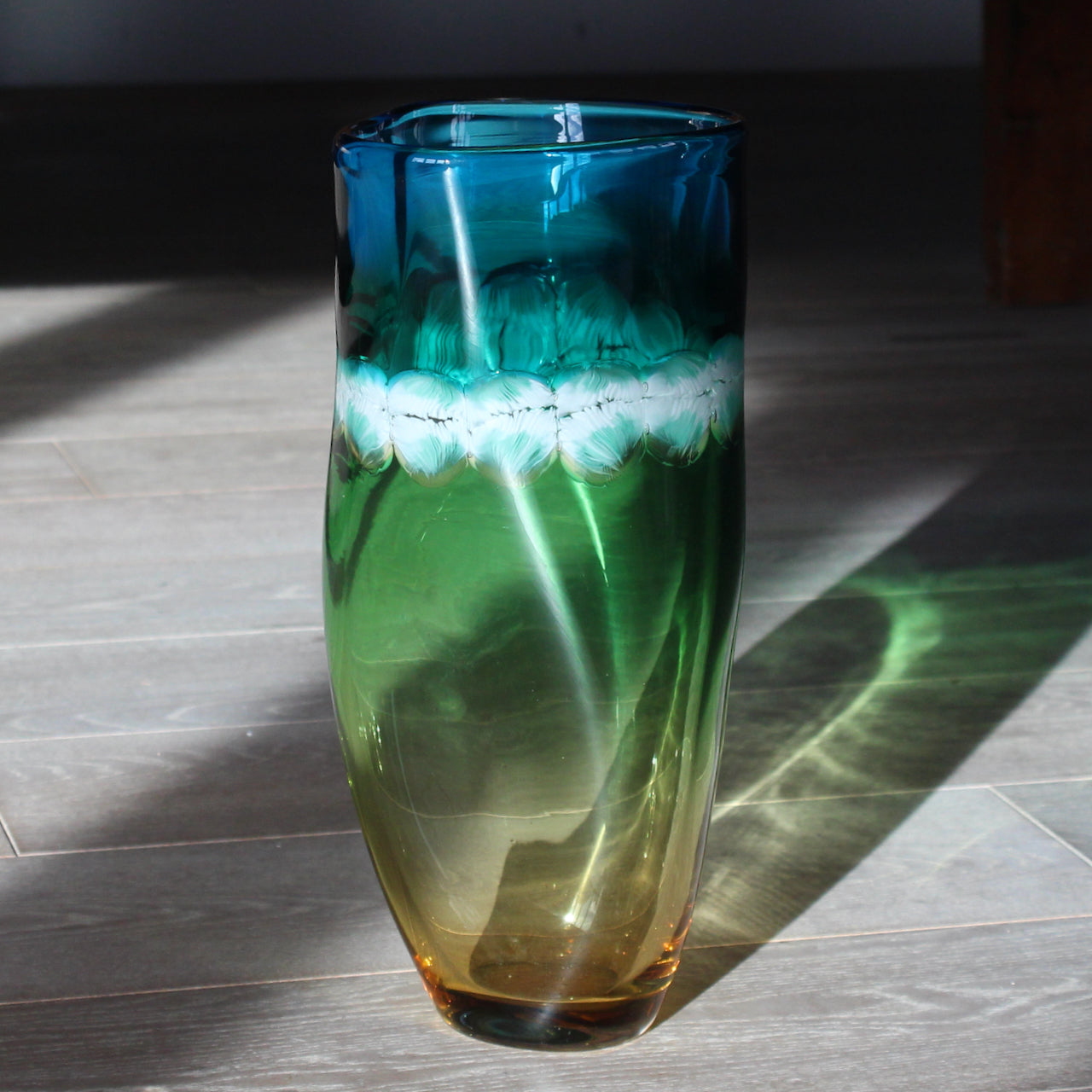 a Benjamin Lintell hand-blown glass vessel in blue, green and amber with a white and turquoise murani detail midway up, it was designed and made by Benjamin in Murano, Italy the glass capital of the world.