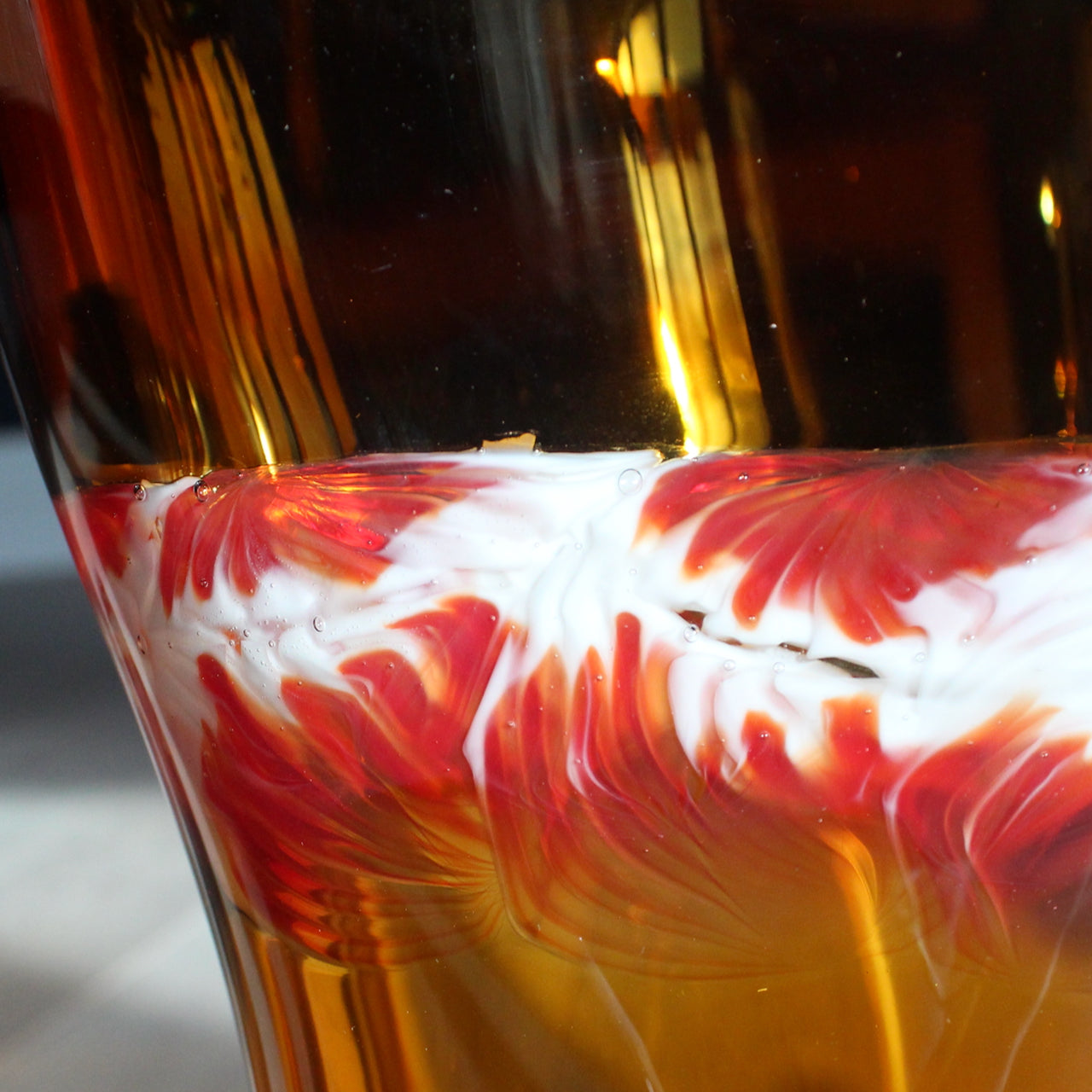 close up detail of Benjamin Lintell hand-blown glass vessel in amber with a white and red murani detail midway up, it was designed and made by Benjamin in Murano, Italy the glass capital of the world.