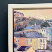 Detail of Jill Hudson framed painting of a Cawsand with colourful rooftops on a dark blue wall.