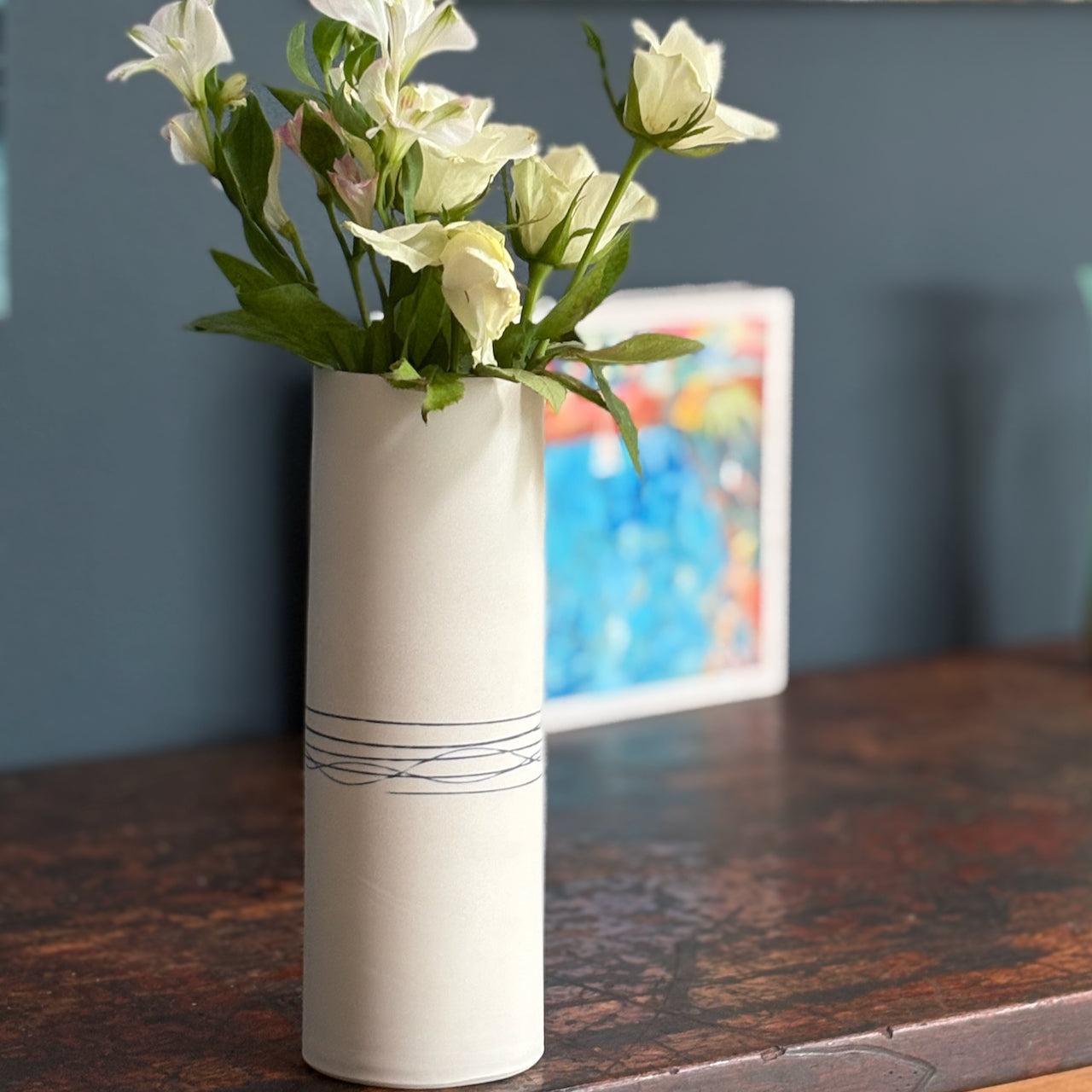 Porcelain Liz O'Dwyer vase with flowers on a wooden surface against a blue wall