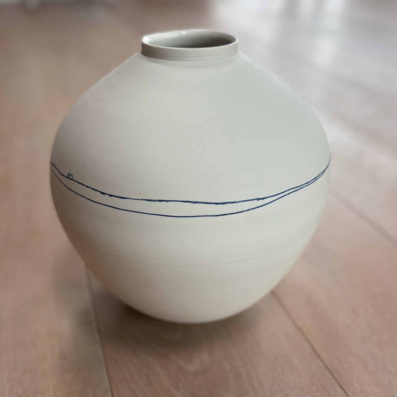 White ceramic moon jar by Liz O'Dwyer  with blue line on a wooden floor