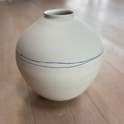 White ceramic moon jar by Liz O'Dwyer  with blue line on a wooden floor