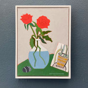 Framed artwork of two red roses in a blue vase on a green surface with a small bag, signed 'Sophie Harding'.