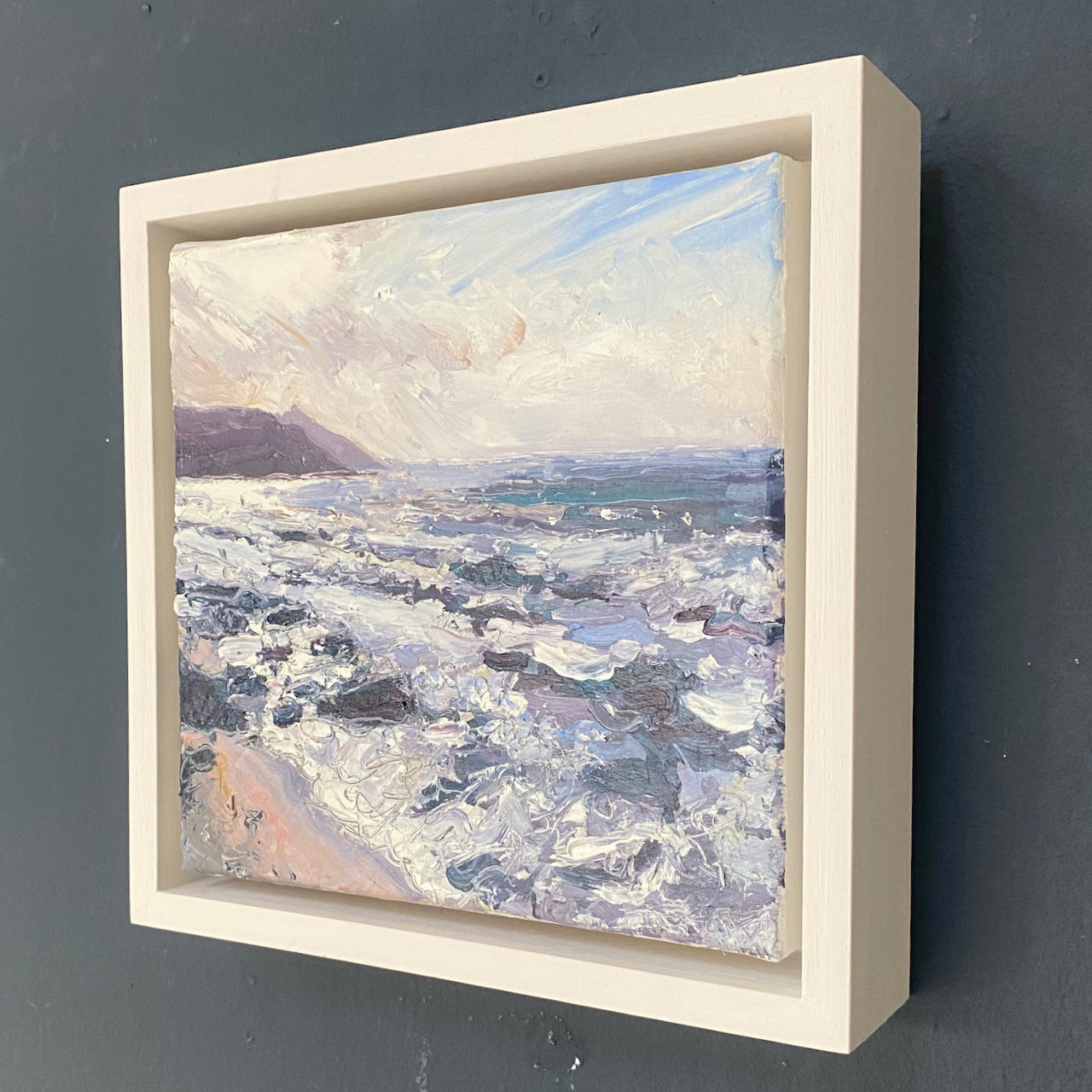 a framed oil painting of Rame Head in south east Cornwall painted from the beach by Jill Hudson, the sea is rough with white waves on greys and purples and the headland is dark against a cloudy sky.