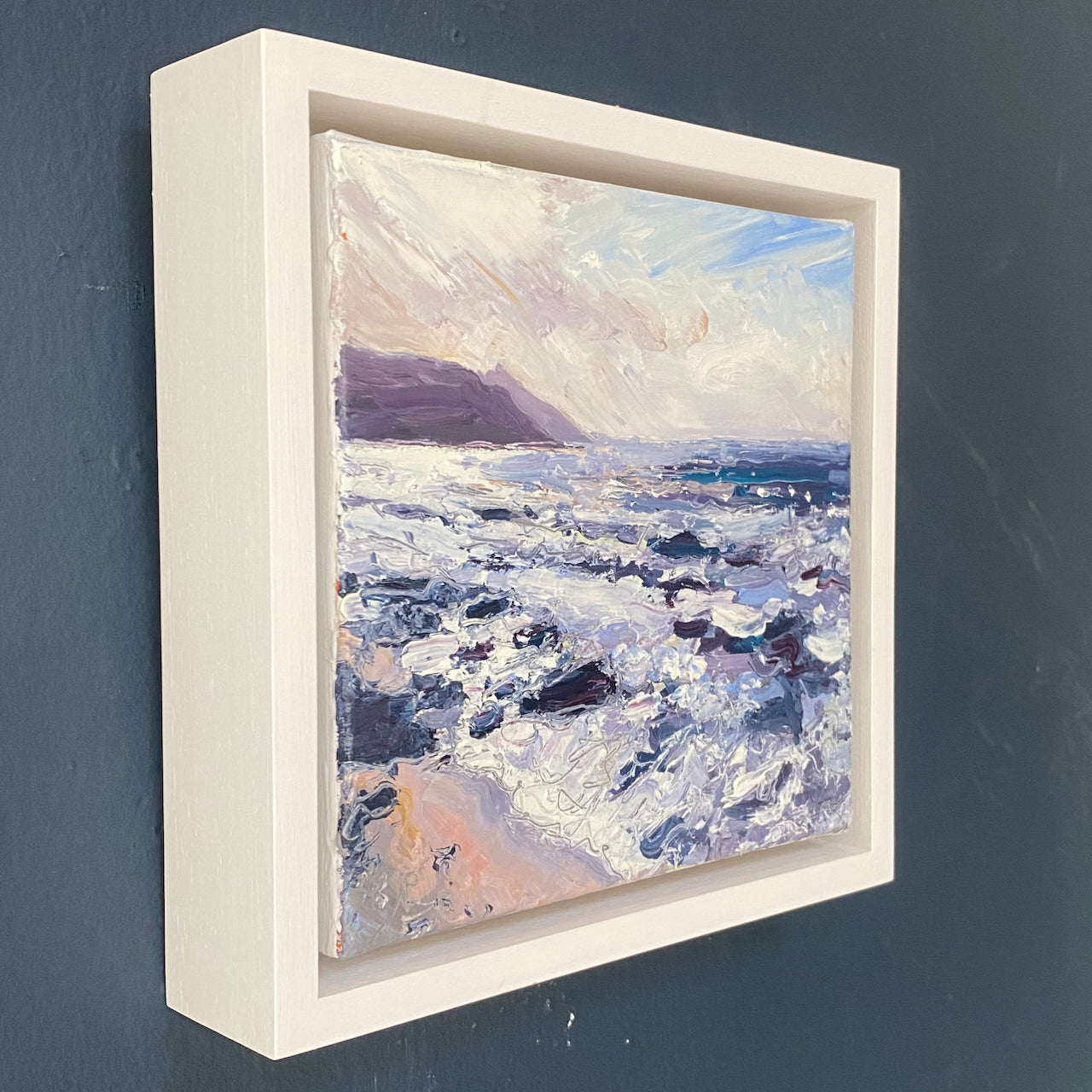 a framed oil painting by  Jill Hudson of Rame Head in south east Cornwall painted from the beach, the sea is rough with white waves on greys and purples and the headland is dark against a cloudy sky.
