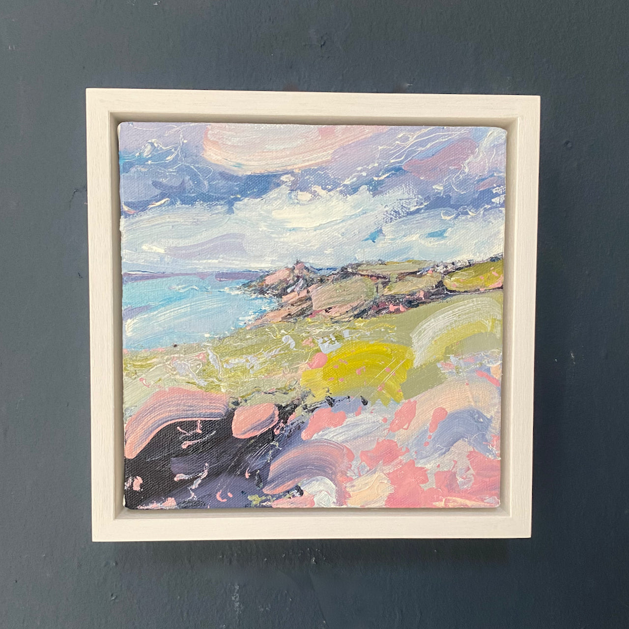 colourful Jill Hudson oil painting of Rame Head in south east Cornwall: the headland is green and pink under a blue sky with white clouds and the foreground has yellow and pink abstract wildflowers 
