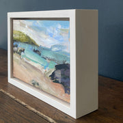 a framed Jill Hudson painting of Rame Head in Cornwall with a golden beach, dark rocks and green headland in the blue sea.