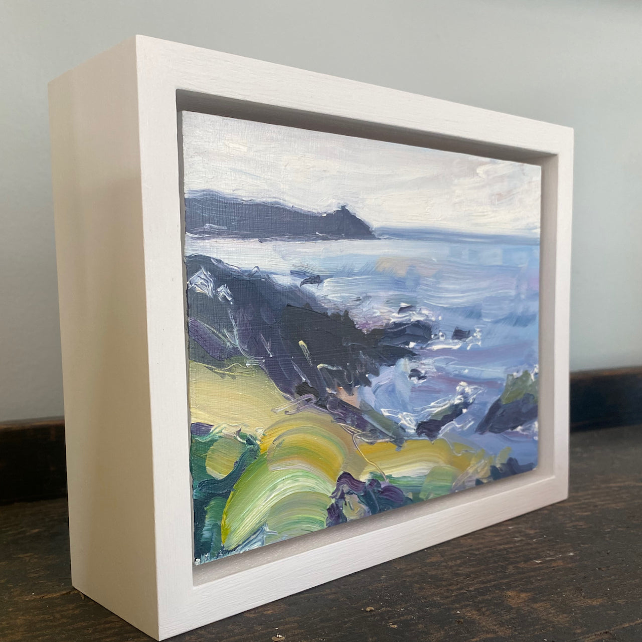a framed Jill Hudson painting of Rame Head in Cornwall with dark skies and a yellow foreground 