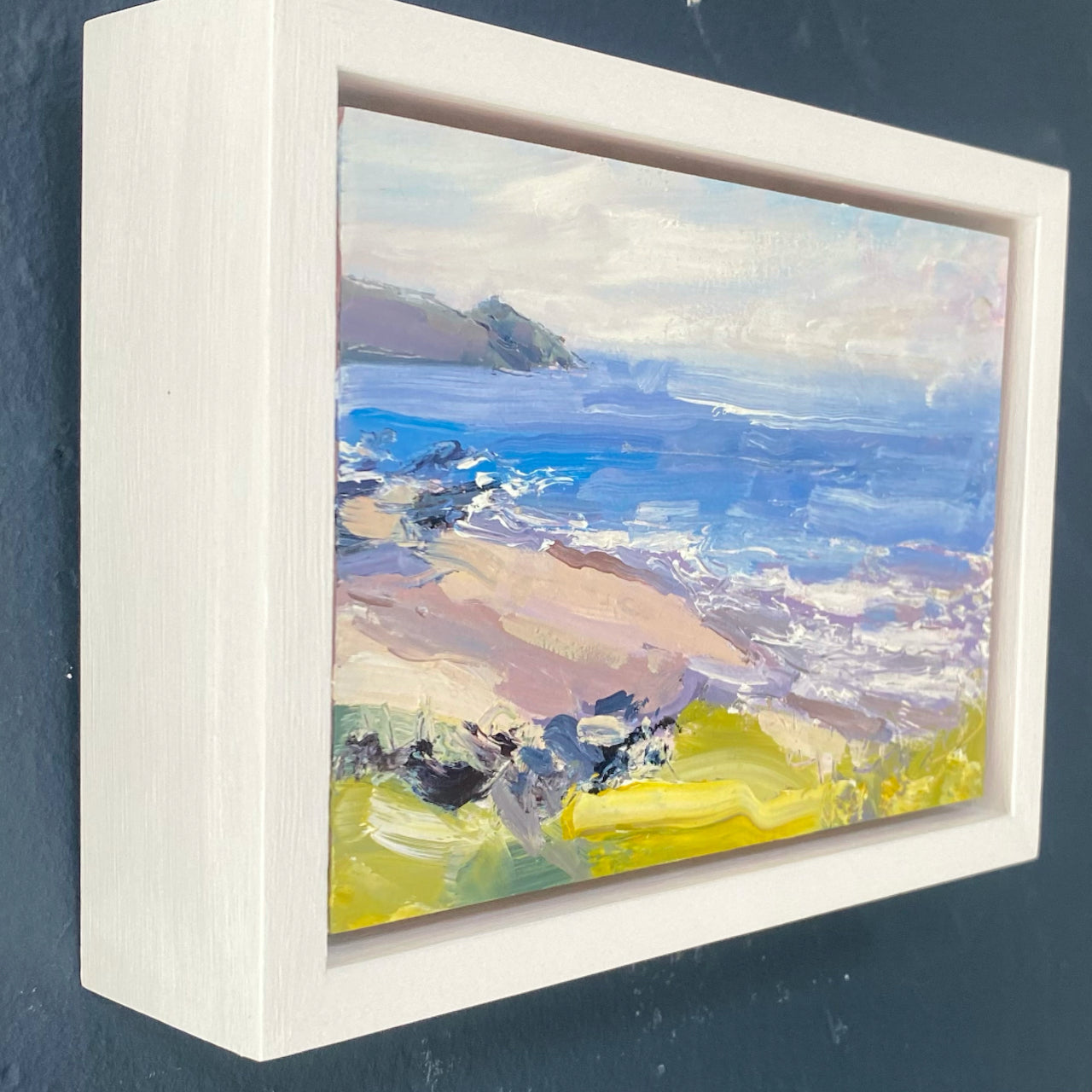 A Jill Hudson painting of Rame Head in Cornwall with a  blue sea, grey sky and pink and yellow coloured beach.