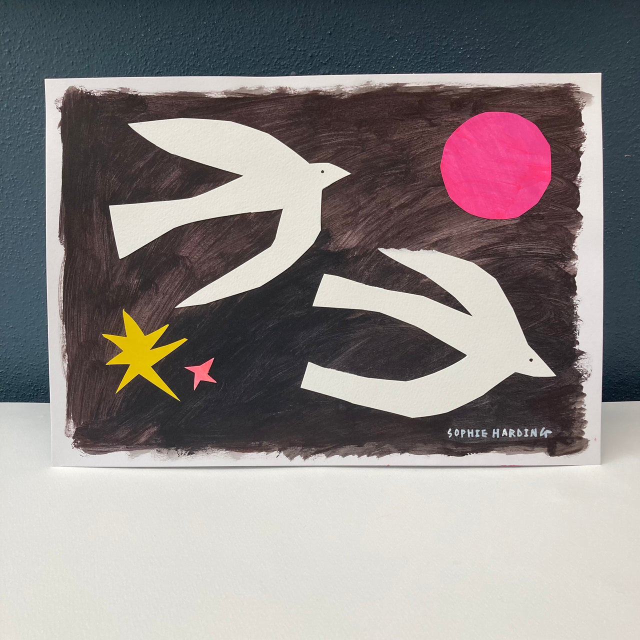 Two white birds on black background, pink moon with yellow and pink star by artist Sophie Harding.
