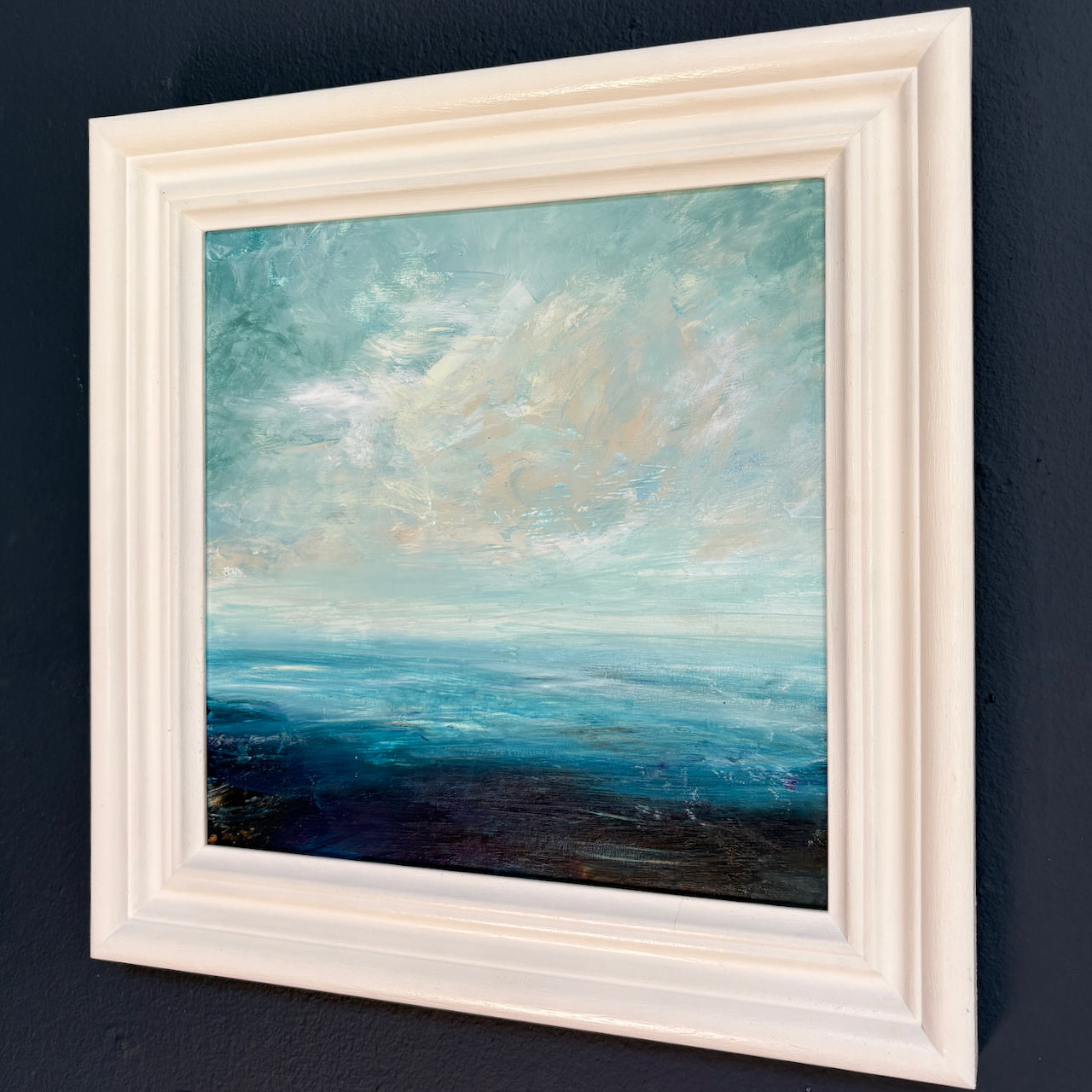 Claire Howlett framed painting of a seascape with blue sky and clouds on a dark background